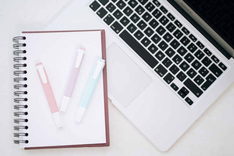 Ein leerer Notizblock mit drei Stiften liegt neben einem Notebook