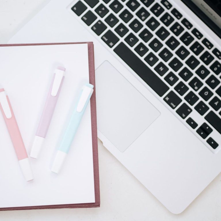 Ein leerer Notizblock mit drei Stiften liegt neben einem Notebook